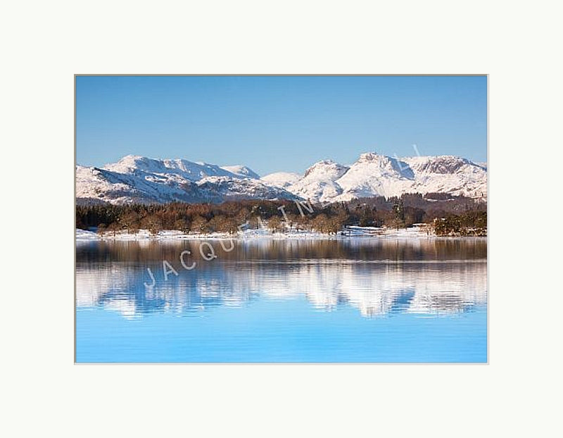 Stunning winter landscape showing snow capped mountains and a perfect reflection in Lake Windermere, lake District. Shown with a white mount