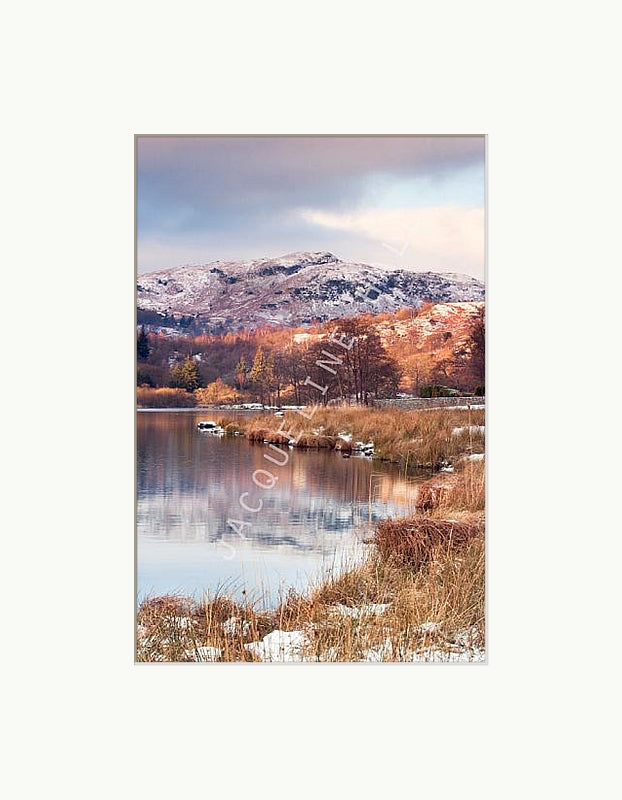 Snow capped winter fells beyond Rydal Water, Lake District with reflections on the waters edge. Shown with a white mount 