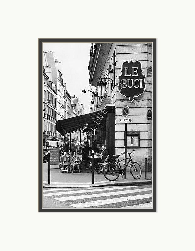 A black and white photograph of the corner of a Le Buci cafe in the Quartier Latin district in Paris. Shown with a double mount of black on the bottom and white on top. 