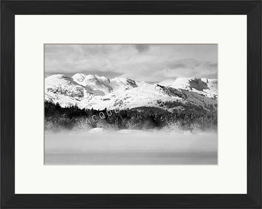 A black and white photograph of Lake Windermere , Lake District showing snow capped mountains and mist of the top of the water. Supplied in a  black frame.