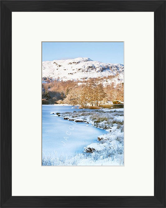 Winter fells and frozen lake at Rydal Water, Lake  District. Shown with a black frame and white mount