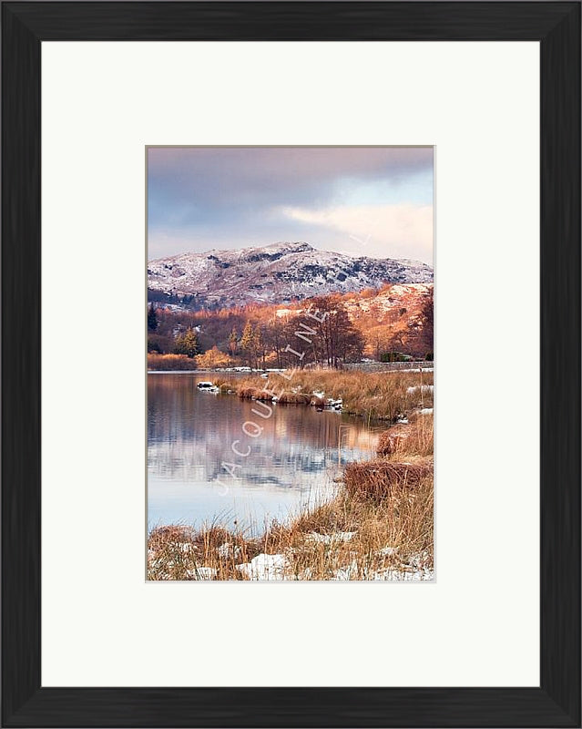 Winter at Rydal Water, Lake District showing snow capped mountains and reflections in the waters edge. Shown with black frame