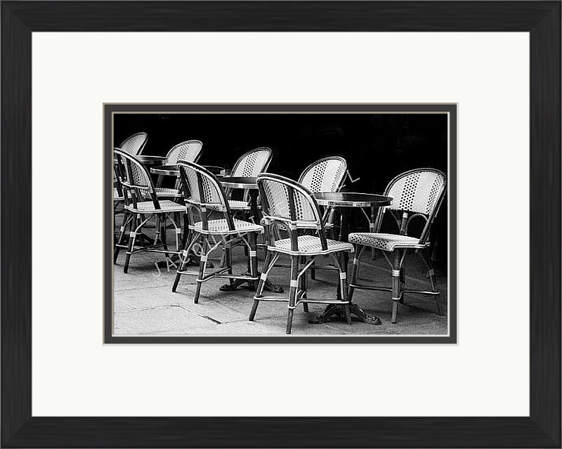 A black and white photograph of cafe table and chairs in the Quartier Latin district in Paris. Shown in a black frame with a double mount of black on the bottom and white on top.