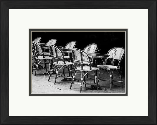 A black and white photograph of cafe table and chairs in the Quartier Latin district in Paris. Shown in a black frame with a double mount of black on the bottom and white on top.